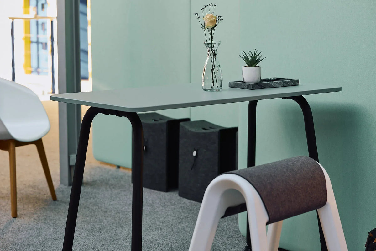 Aufgeräumter Schreibtisch mit Vase und Zimmerpflanze vor mintgrüner Wand