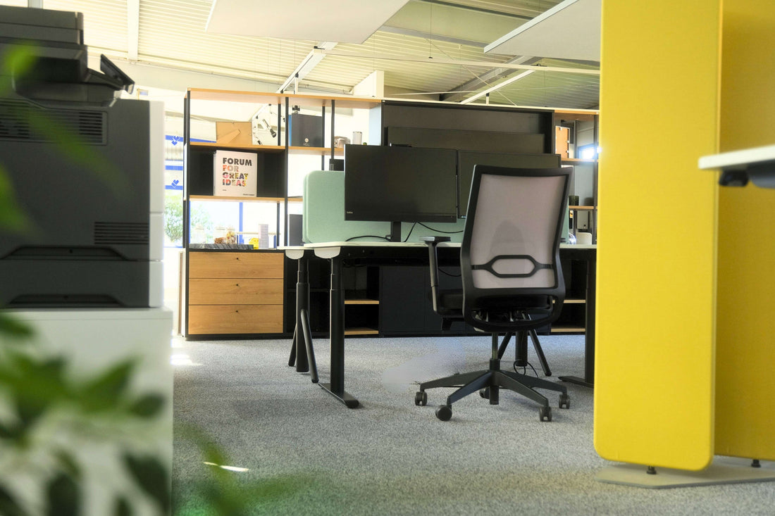 Arbeitsplätze mit höhenverstellbaren Tischen, gelber Akustikwand und Multifunktionsdrucker