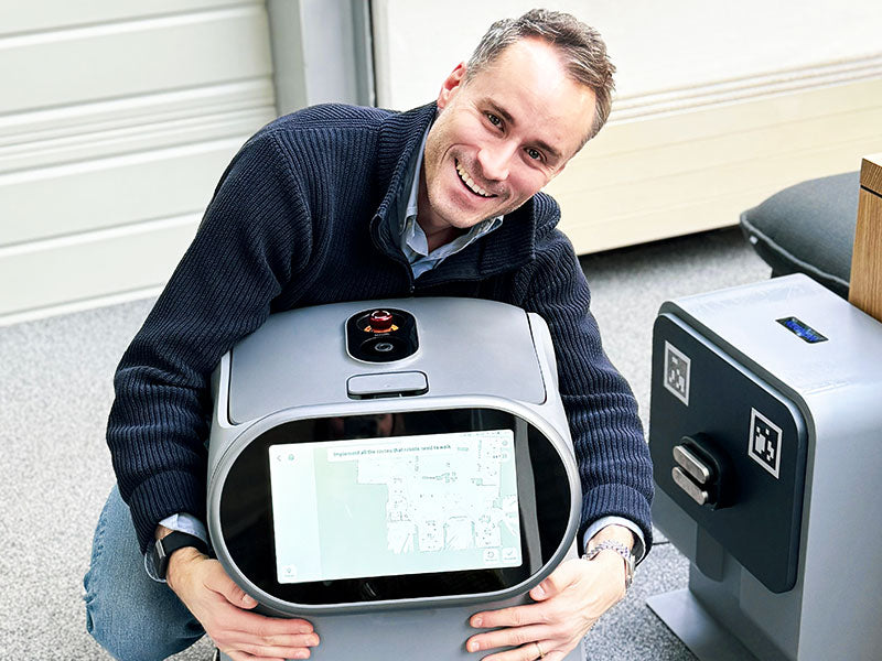 Mitarbeiter kniet lächelnd neben einem Serviceroboter mit Touchdisplay