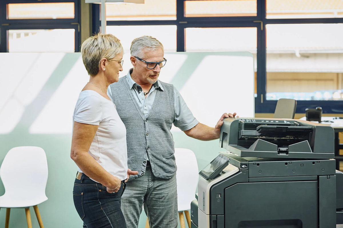 Zwei Mitarbeitende bedienen einen Multifunktionsdrucker im Büro