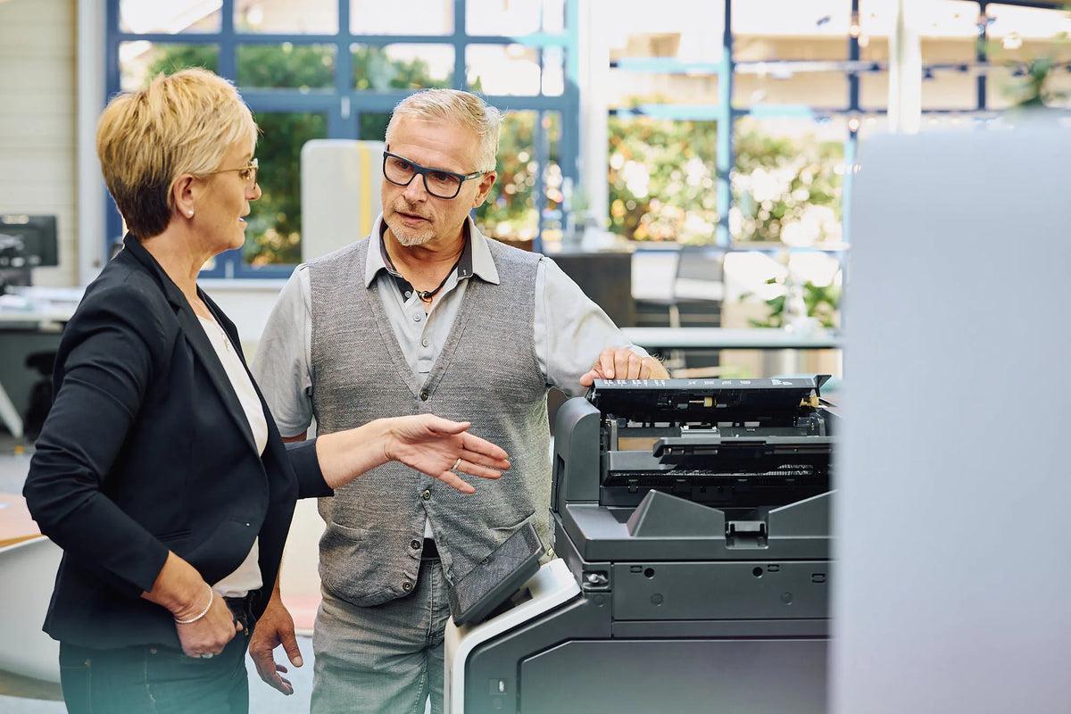 Zwei Personen im Gespräch neben einem Multifunktionsdrucker