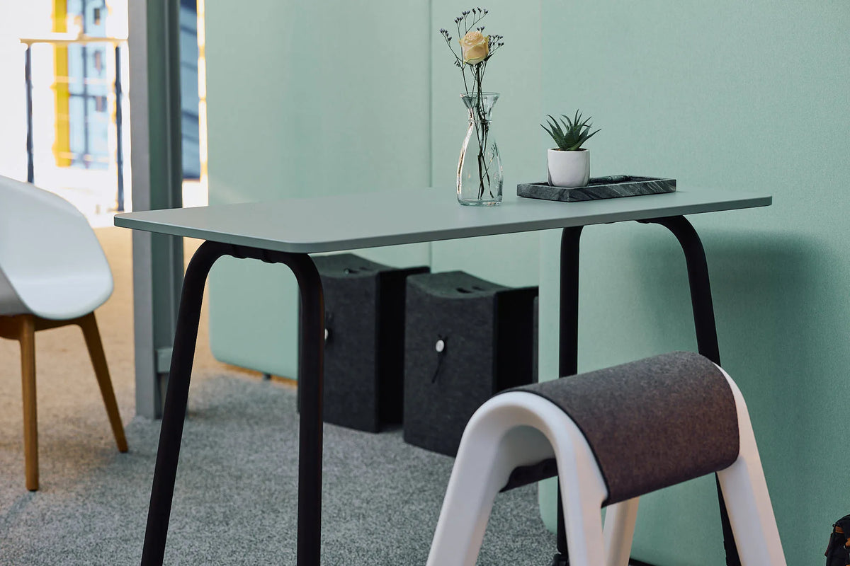 Aufgeräumter Schreibtisch mit Vase und Zimmerpflanze vor mintgrüner Wand