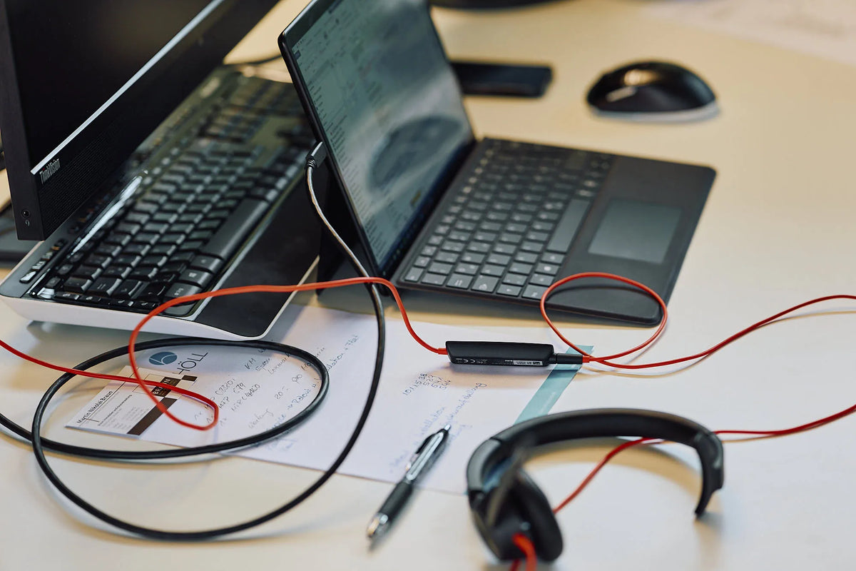 Laptop und Monitor auf einem Schreibtisch mit Netzwerkkabeln und Headset