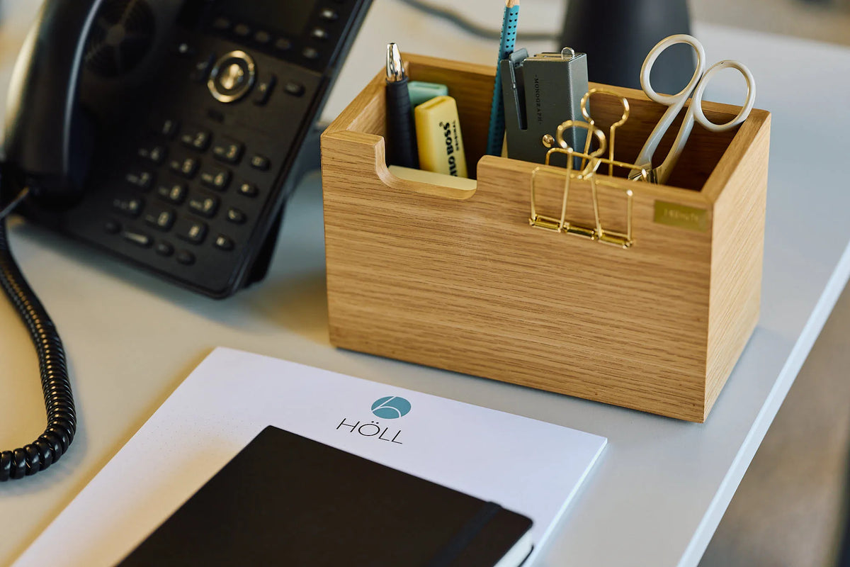 Holz-Stiftebox mit Schere und Klammern neben einem Tischtelefon