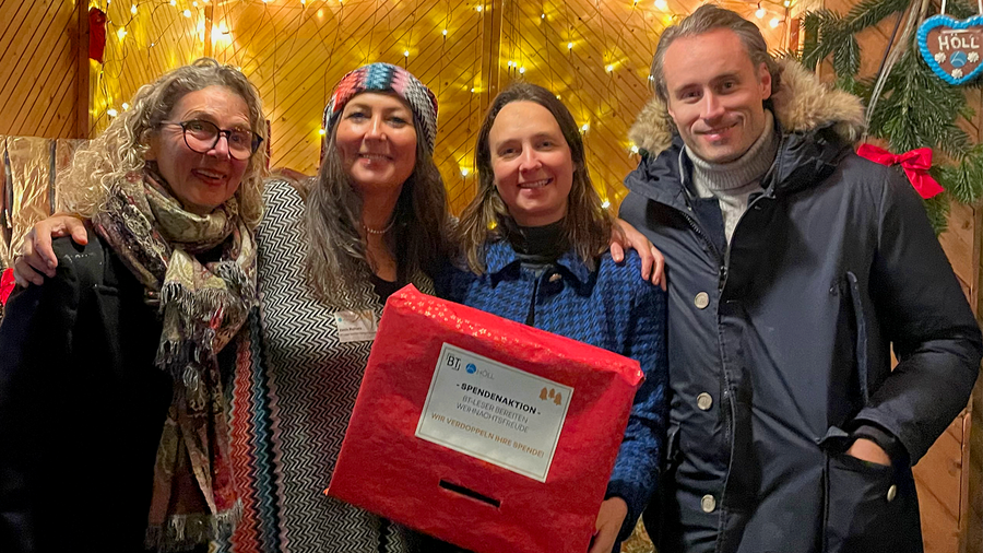 Vier Personen mit einer roten Spendenbox vor einer Lichterwand