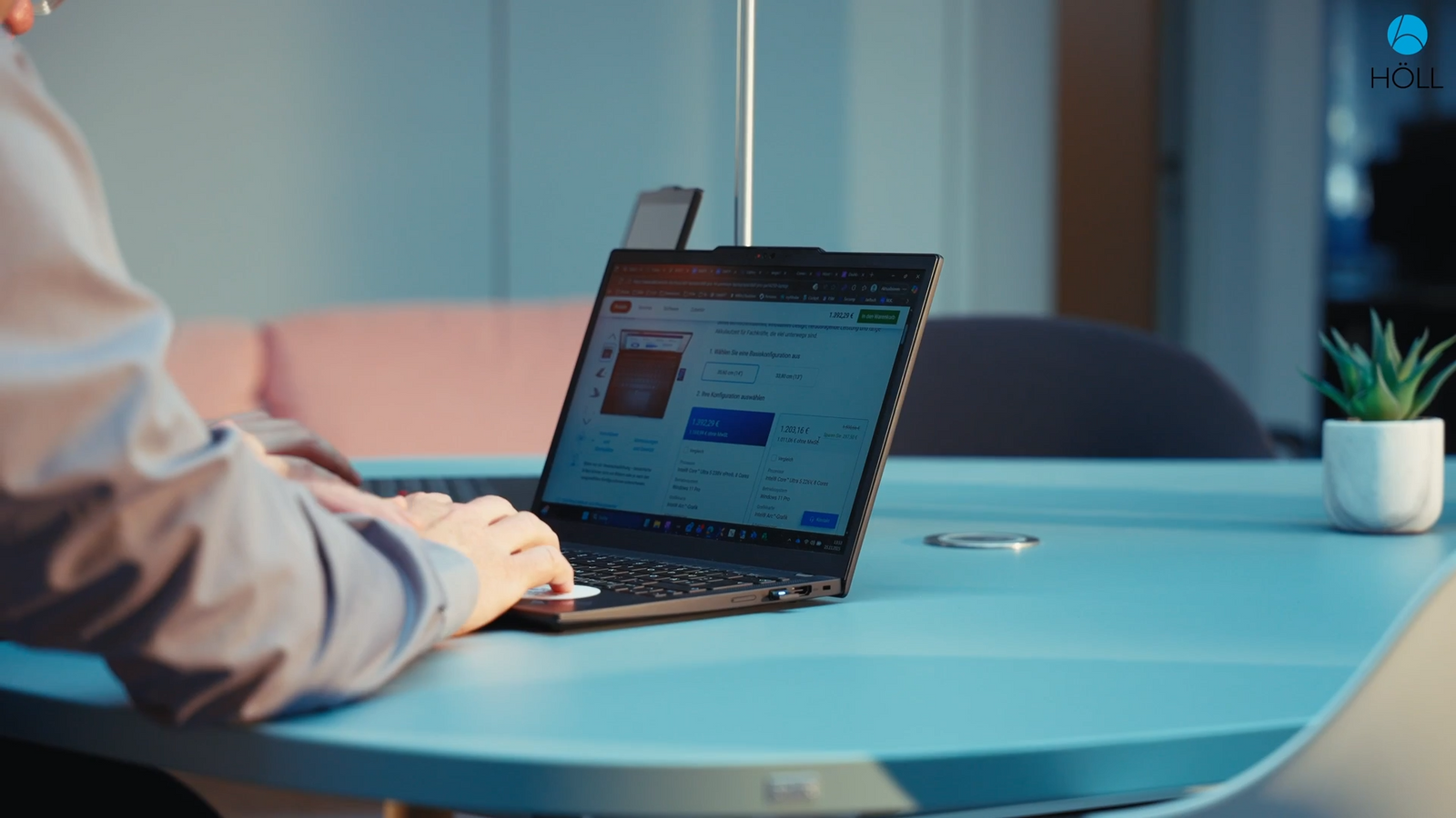 Hände tippen an einem Laptop auf einem hellblauen Tisch